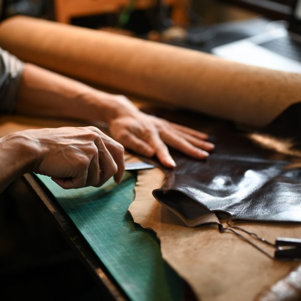 Close up view of craftsman skillfully using a cutting tool to shape the leather.